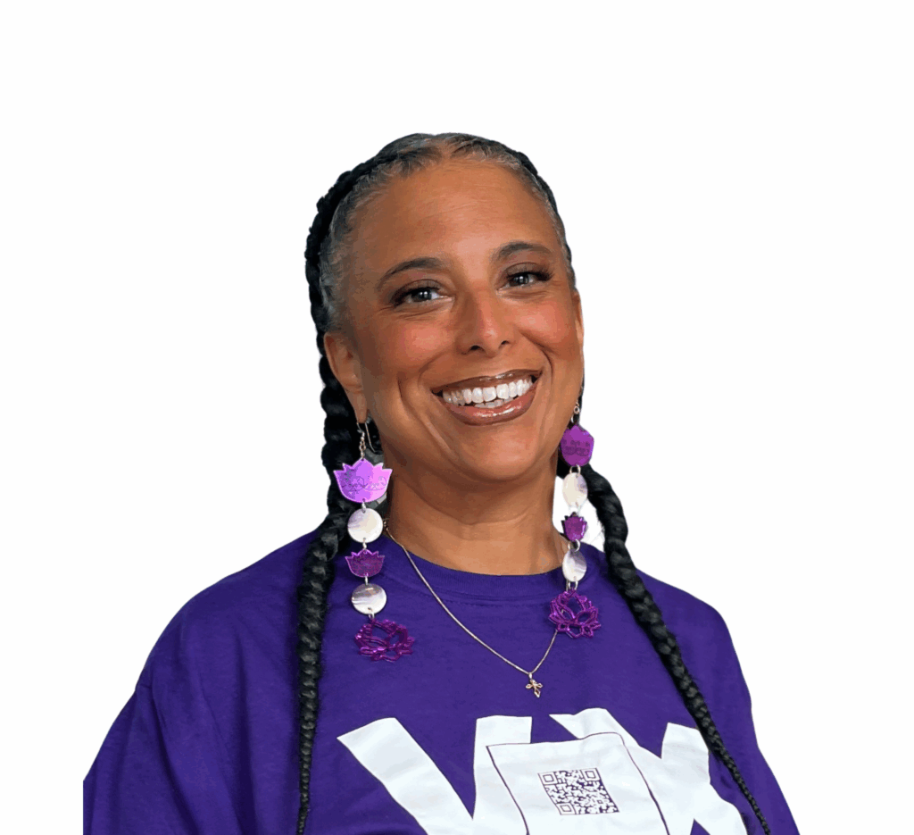 Maria Hendricks, An AfroIndigenous woman with long dark box braids, brown skin, dark brown eyes and a purple Vox top, warmly smiles at the camera.