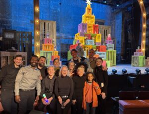 a large group photo of Deaf community, including Deaf DASLs, Deaf and hearing audience, ASL Interpreting team, family and friends standing together in front of the stage at Cutler Majestic Theater.